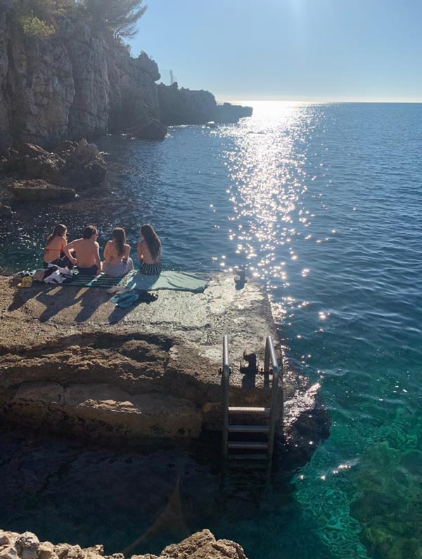4 study abroad students sitting on a rock looking at the water in front of them