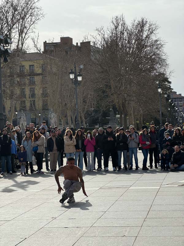 A person dancing on a city square surrounded by a crowd of onlookers