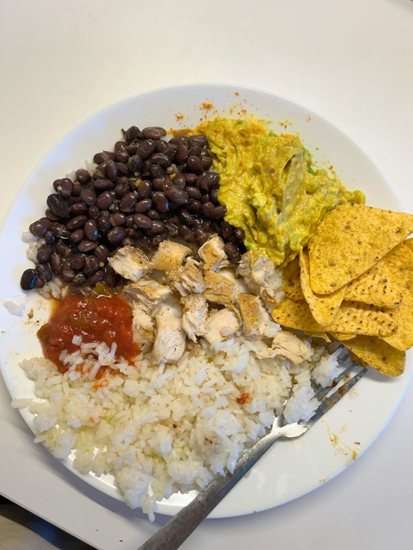 A plate of black beans, salsa, chicken, white rice, guacamole, and corn chips