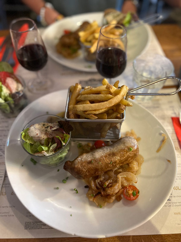 A dish of food on a table featuring a sausage, salad, and French Fries