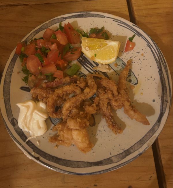 A plate of food featuring fried squid, a slice of lemon, and chopped tomatoes