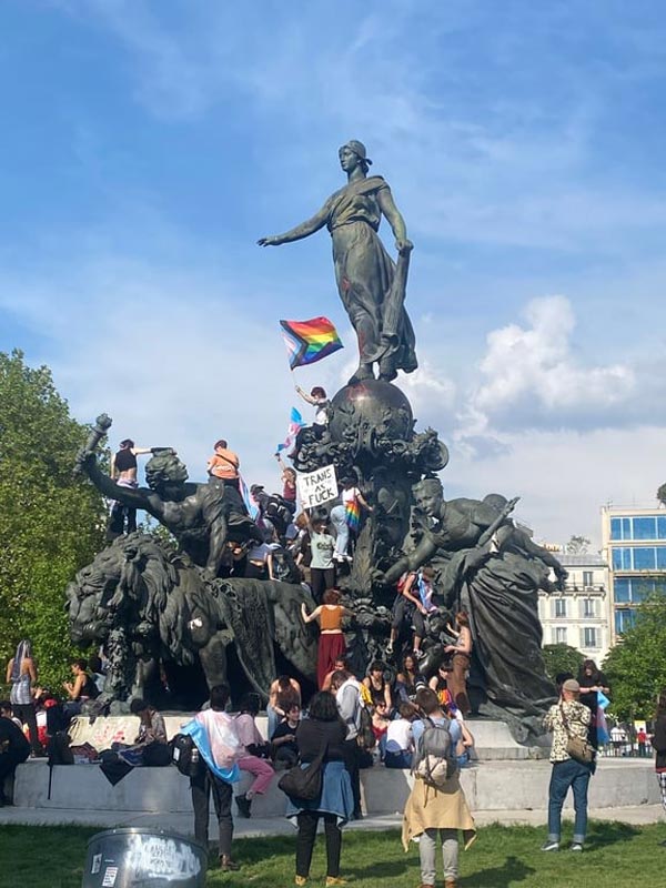 A group of people sitting around a statue with pride swag