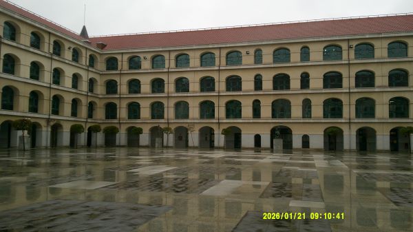The exterior of a building with many orderly windows, a red roof, and smooth pavement in front of it