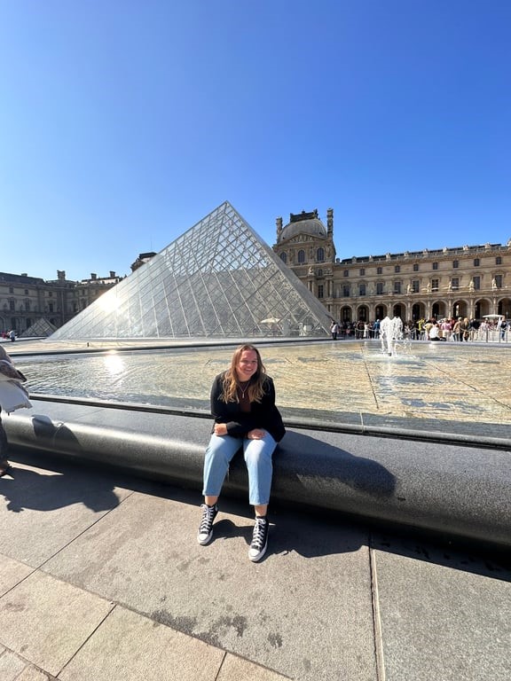 A person sitting on a ledge in front of a glass pyramid