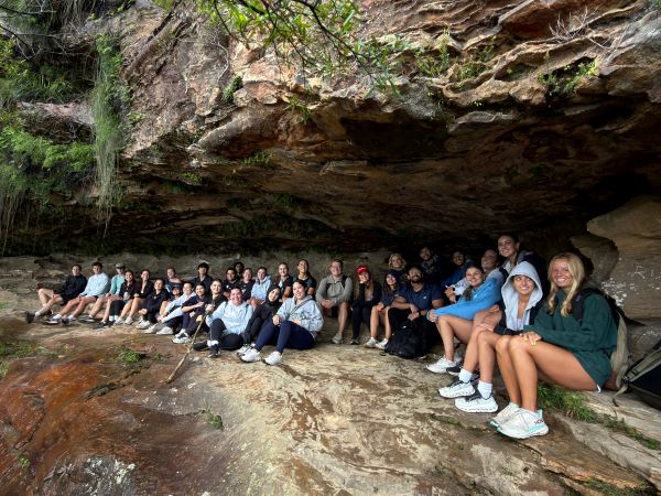 A large group of study abroad students sat inside a cave structure and smiling at the camera
