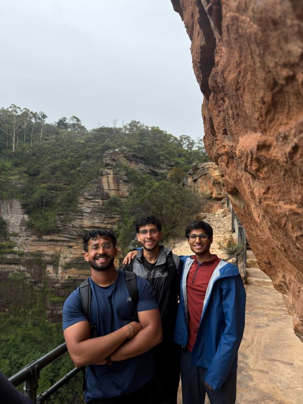 Three study abroad students standing on a hiking trail in front of a mountainous landscape and smiling at the camera