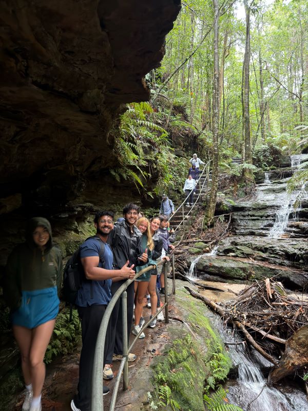 A group of study abroad students smiling for the camera in front of a set of stairs in a wooded area