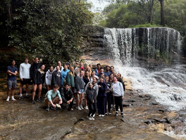 A large group of study abroad students standing in front of a small waterfall and smiling at the camera