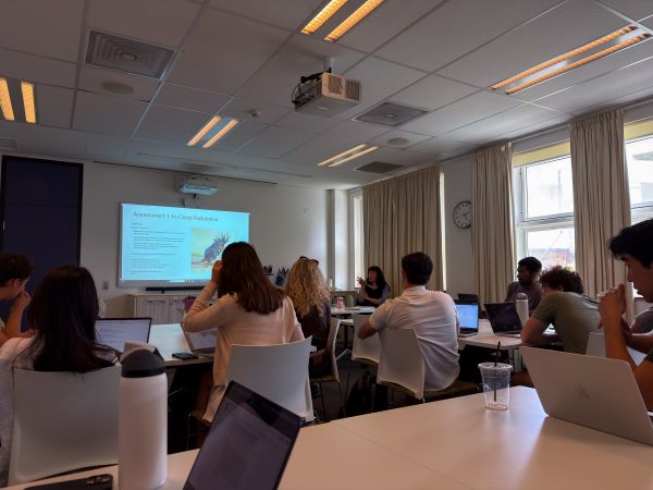 The interior of a classroom with study abroad students sitting in chairs and looking at a seated professor at the front of the room