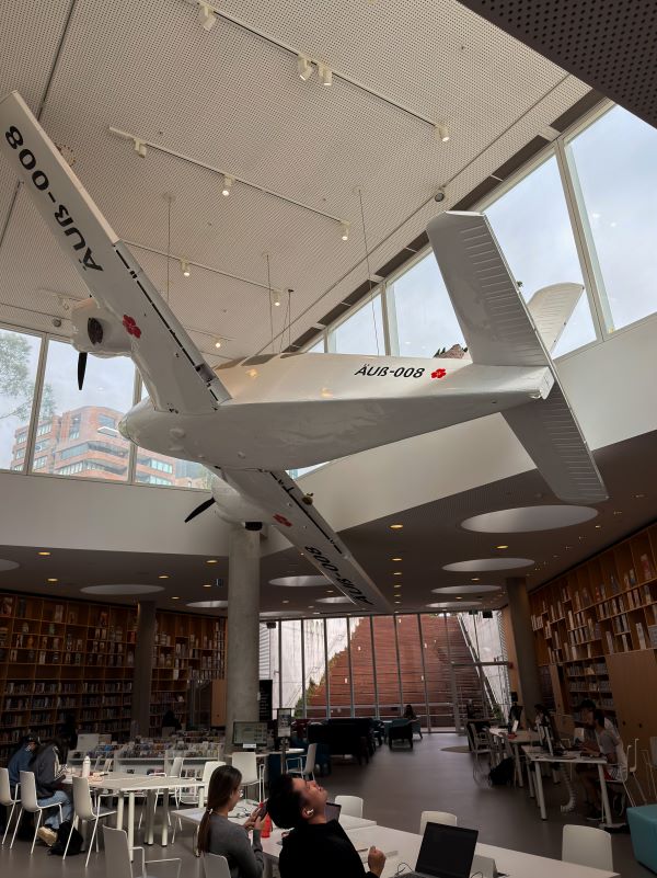 The interior of a library featuring a large airplane sculpture hanging suspended over tables