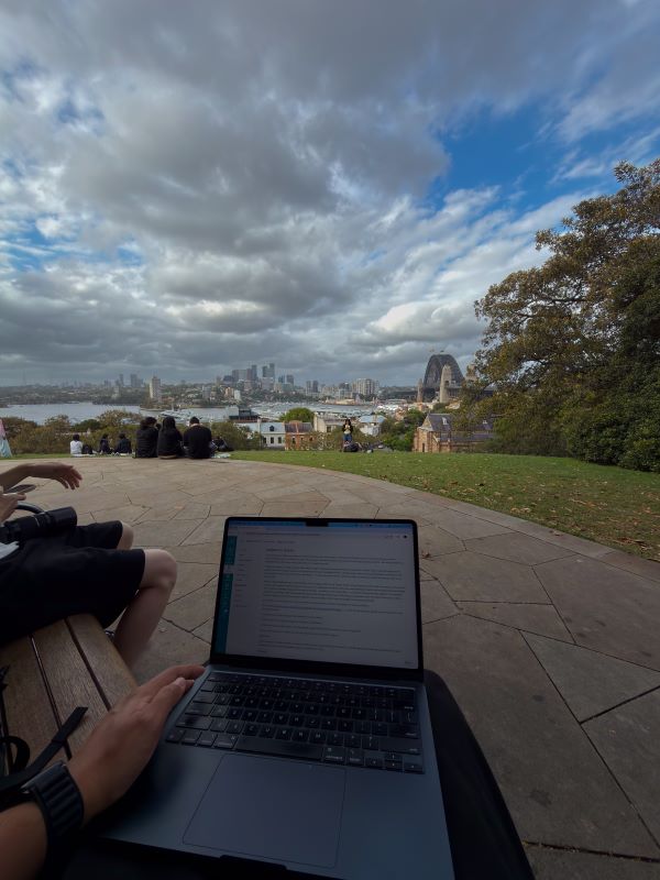 A view from above of a body of water alongside city buildings and a large bridge, behind a laptop sitting on a study abroad student's lap