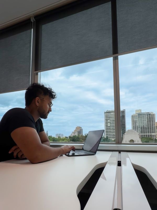 A study abroad student seated at an indoor desk working on a laptop in front of a large window
