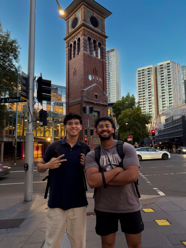 Two study abroad students standing on a city sidewalk in front of a tall building and smiling at the camera