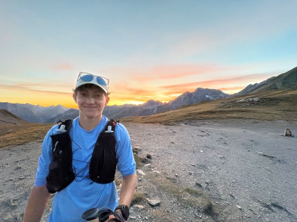 A study abroad student wearing a blue shirt smiling at the camera in an outdoor mountainous setting
