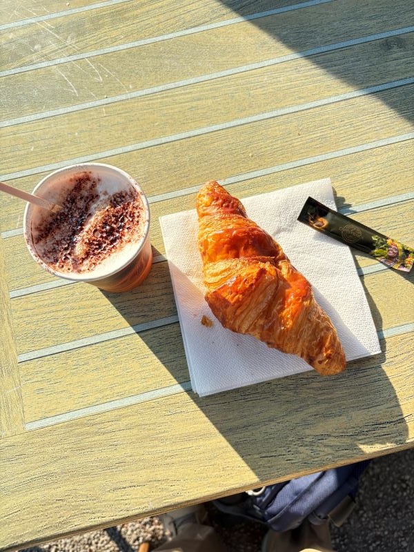 A croissant on a napkin and a cup of coffee sitting on a tabletop outdoors