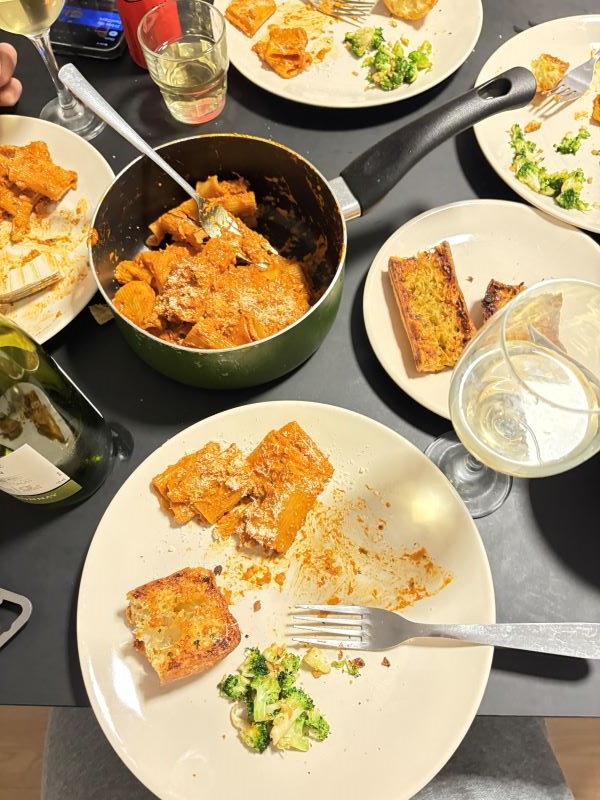 A table full of plates of food including pasta, broccoli, and slices of toasted bread