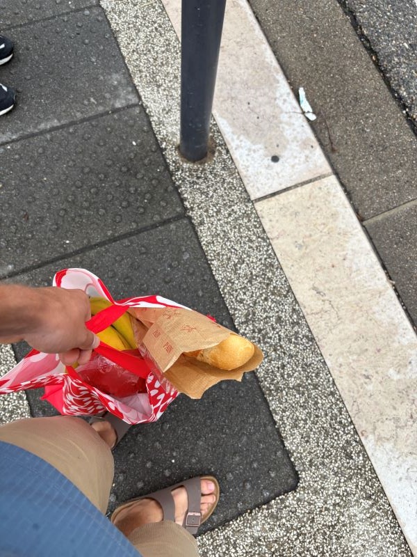 A view from above of a hand holding a bag of groceries above a pair of feet on a sidewalk