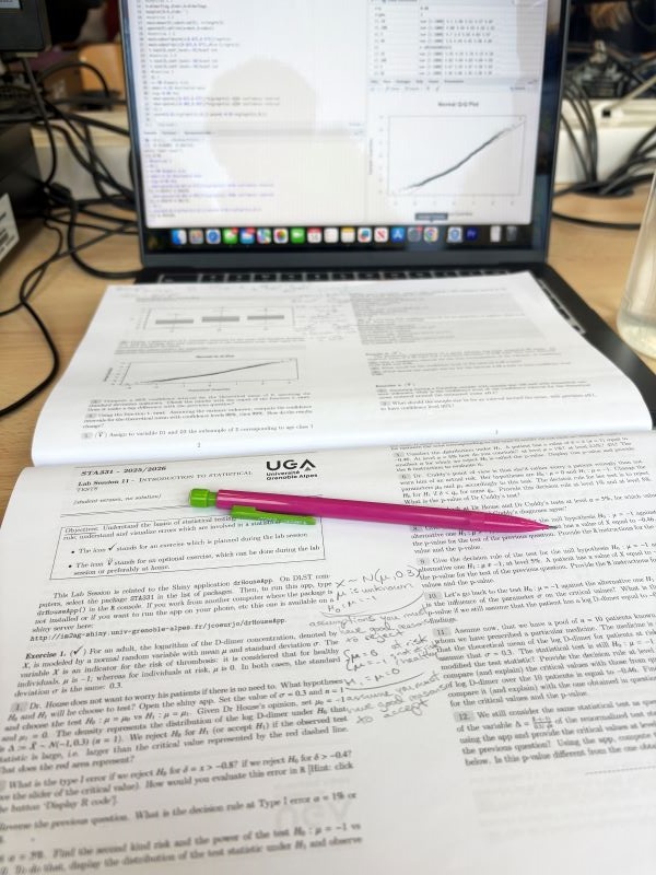 An open textbook and a mechanical pencil resting on top of a laptop open to reveal a graph and text on its screen