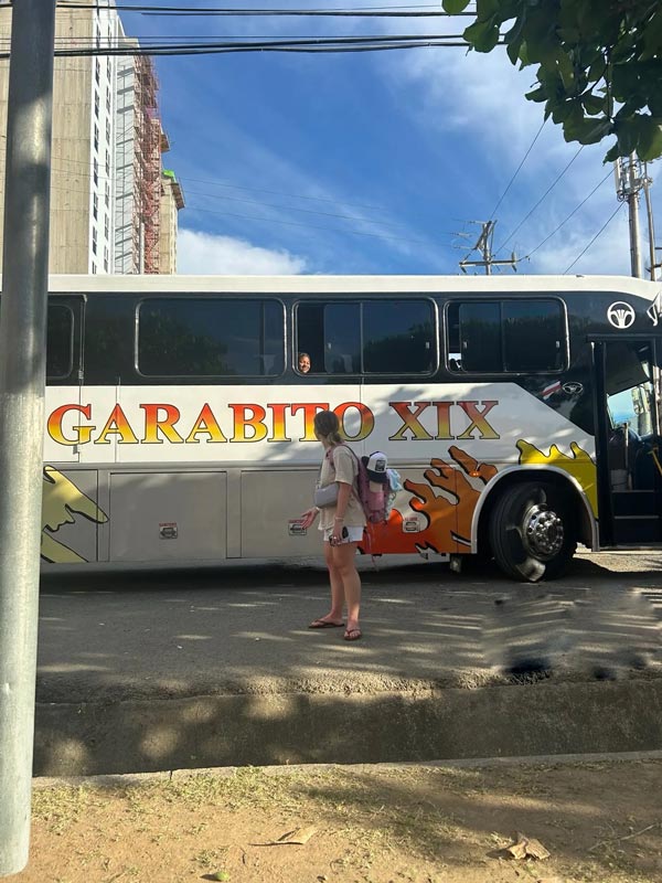 A study abroad student standing next to a bus talking to another student inside the bus