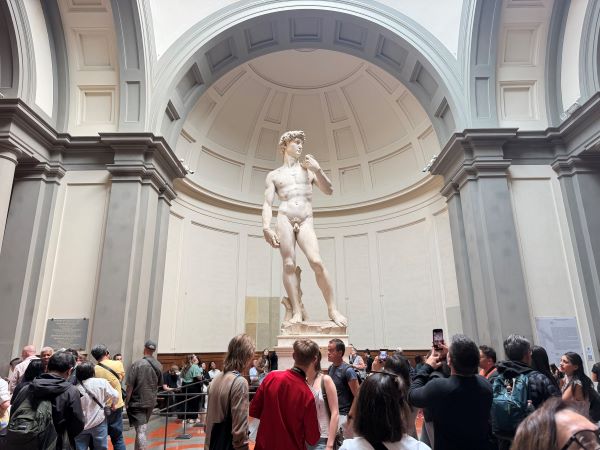 A large statue of a man standing on a pedestal in an indoor room crowded with people