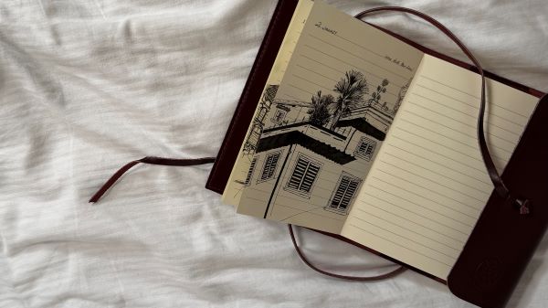 A notebook open to a page with a detailed ink drawing of a building and trees
