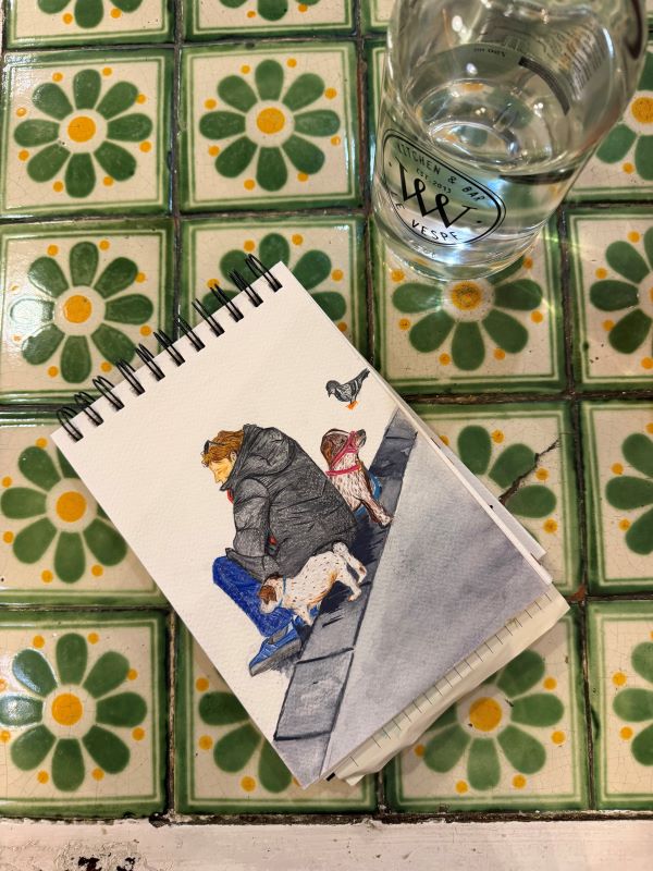 A small sketchpad featuring a drawing of a woman seated between two small dogs