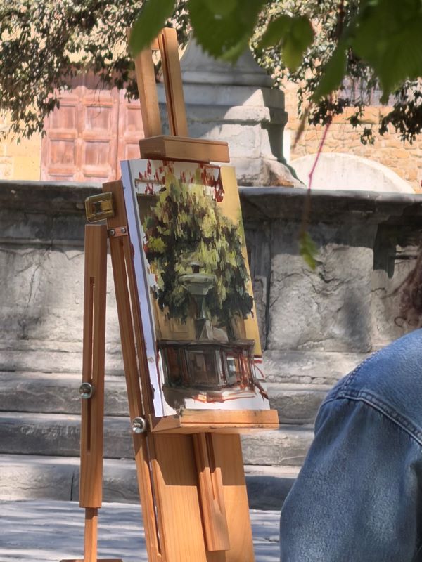 A colorful painting of a fountain displayed on a wooden easel outdoors