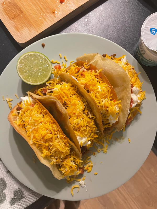 A plate of tacos with cheese and a lime wedge