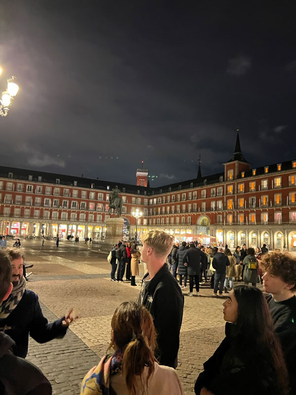 A group of study abroad students in a plaza with Plaza Mayor, Madrid in the background