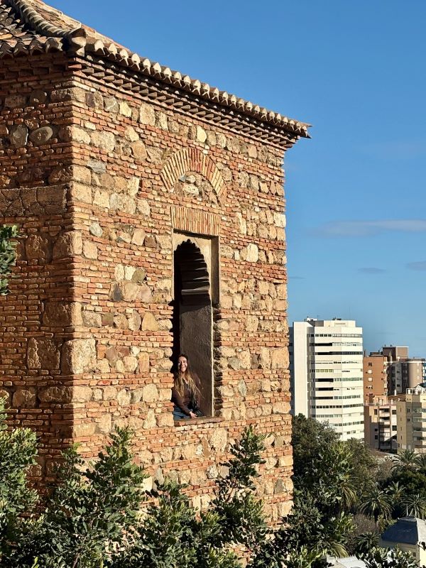A study abroad student smiling at the camera from the arched window of a stone building