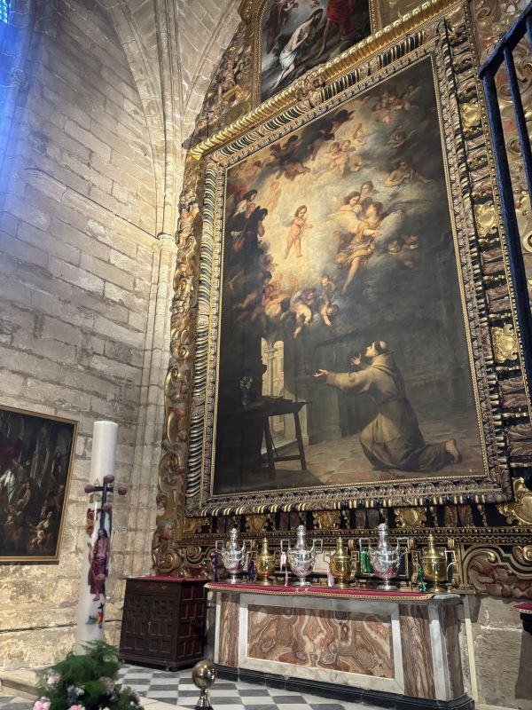 A large painting of a man on his knees looking up to angels above, hung inside an ornately decorated indoor space
