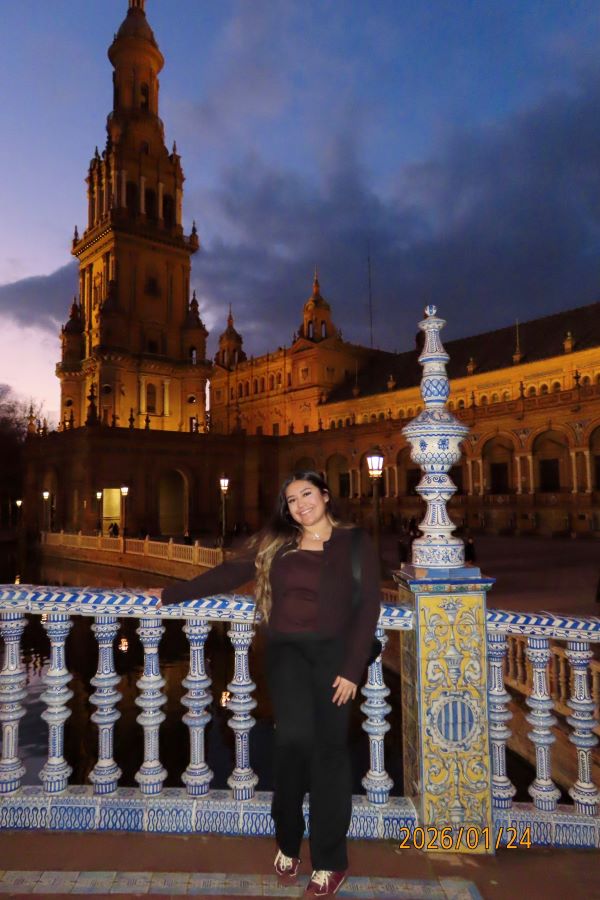 A study abroad student standing outdoors in front of an ornately decorated banister and smiling at the camera