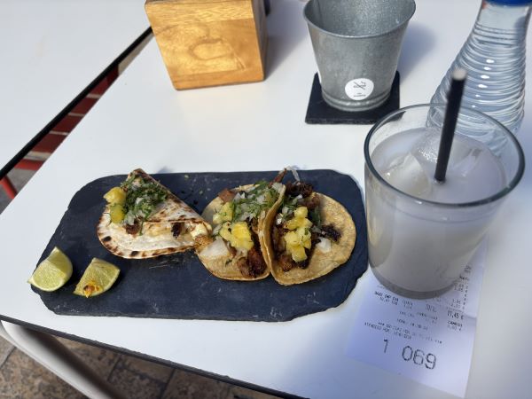 Three tacos on a small black plate seated next to a milky white drink on a white table