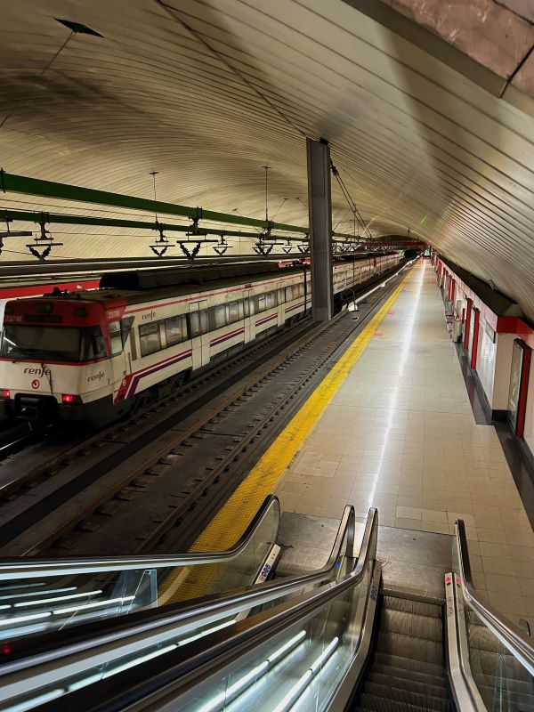 An escalator leading down onto an empty metro platform, with a white train to the lefthand side