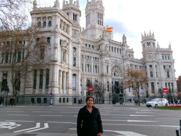 A study abroad student smiling at the camera and standing in front of a large intricately-designed white building