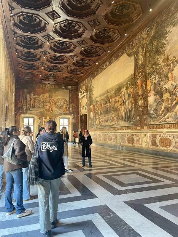 A group of study abroad students in a large room looking at paintings on the walls