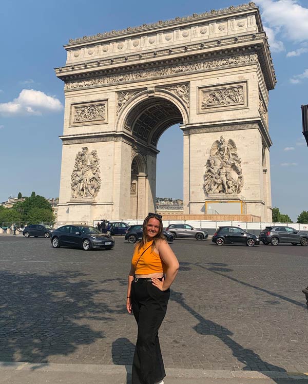 A study abroad student standing in front of a large stone arch