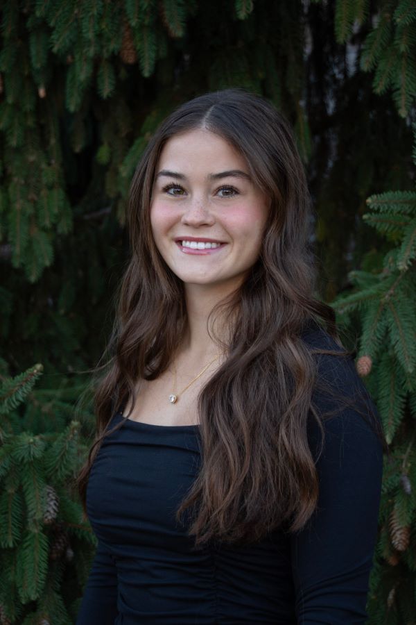 A study abroad student with long wavy brown hair wearing a black long-sleeved shirt and smiling at the camera