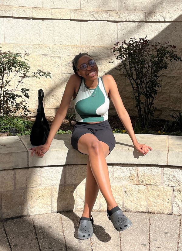 A study abroad student sitting on a stone structure outdoors with one leg crossed over the other and smiling at the camera