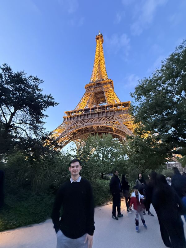 A study abroad student standing in front of the Eiffel Tower and smiling at the camera