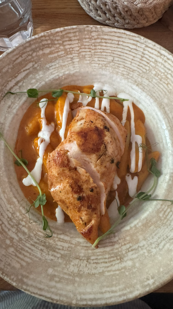 A chicken dish covered in an orange sauce sitting in a cream-colored plate on a table