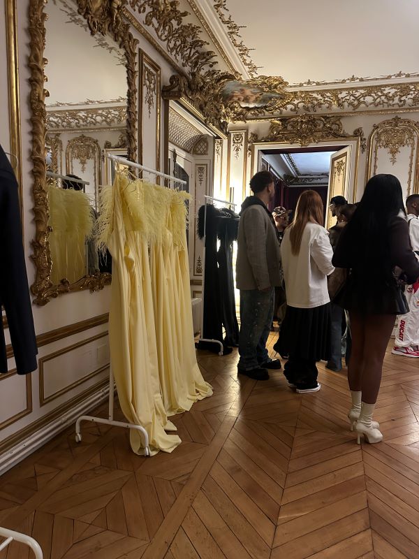 Several butter-yellow garments on a rack near a group of people standing and looking away from the camera in an indoor setting