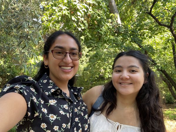 Two study abroad students smiling and taking a selfie outdoors under a canopy of green leafy tree branches