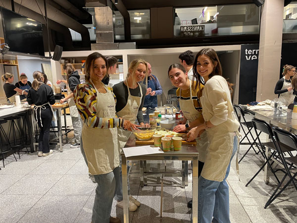 A group of study abroad students in aprons standing around a table with food