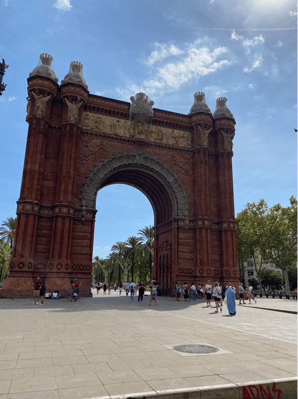 A large archway with people walking around with Arc de Triomf in the background