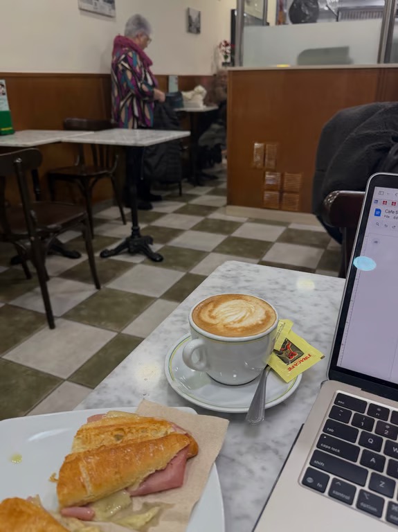 A cafe table featuring a half-eaten sandwich, a full cup of coffee, and a laptop