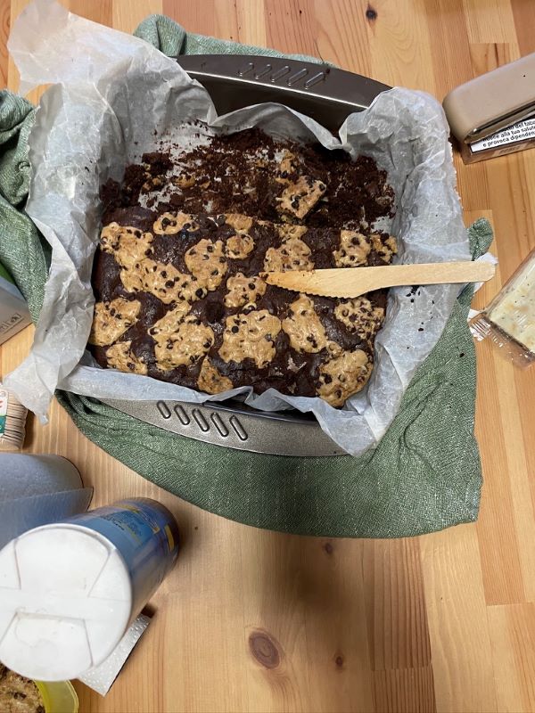 A baking tray sat on a wooden table and half filled with a cookie-brownie dessert