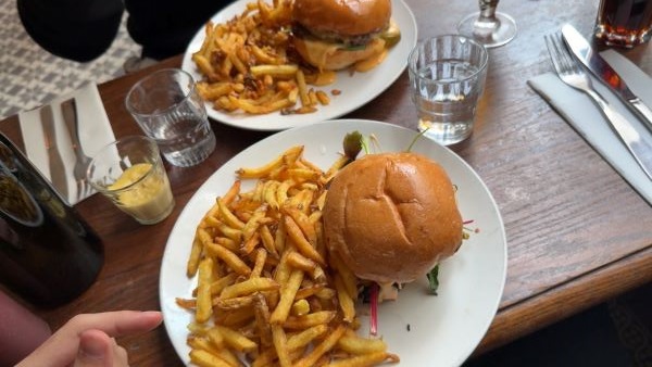 A burger and French fries sitting on a white plate on a wooden restaurant tabletop