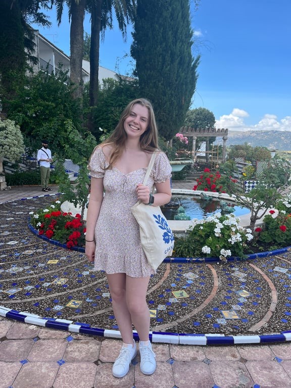 A person standing smiling near a fountain
