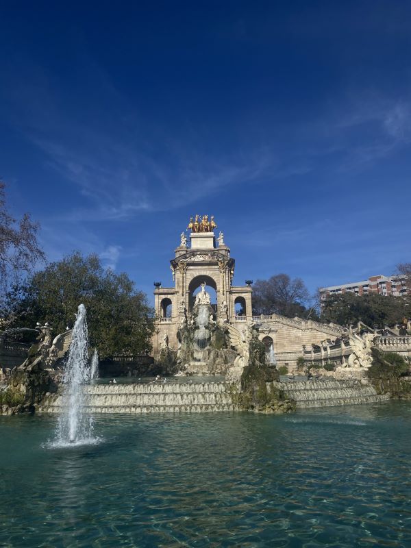 A large outdoor intricate fountain behind a blue body of water
